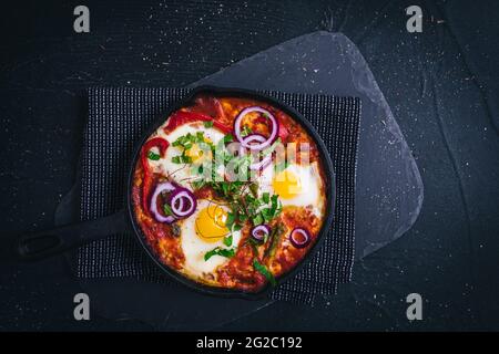 Shakshuka dans une poêle à repasser. Plat traditionnel du Moyen-Orient. Œufs frits avec tomates, poivron, légumes et herbes, œufs ensoleillés. Vue de dessus, Banque D'Images