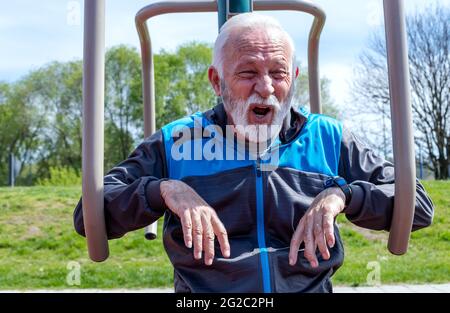 Un homme âgé épuisé qui attrape un souffle après avoir fait de l'exercice sur l'équipement de salle de sport publique en plein air. Banque D'Images