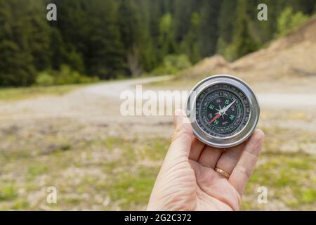 Main d'un alpiniste tenant une boussole avec un champ vert sur l'arrière-plan Banque D'Images