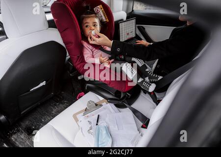 Bébé fille assis dans le siège de voiture pendant que la mère utilise un ordinateur portable Banque D'Images