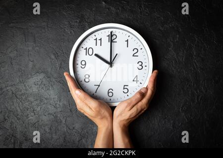 Horloge murale sur les mains de l'homme sur l'arrière-plan de texture noire. Concept de temps de circulation Banque D'Images