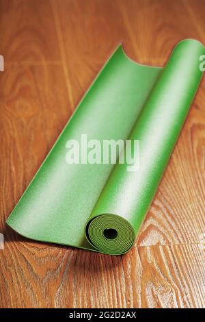 Un tapis de yoga vert est disposé dans un rouleau sur le plancher de bois. Un mode de vie sain et isolé. Banque D'Images