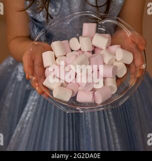 Photo d'une petite fille avec robe bleue offre des bonbons colorés pour l'accueil à la maison dans la fête, donnant des bonbons à l'invité de la maison comme un compliment Banque D'Images