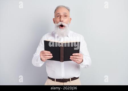 Photo de l'étonnant choqué vieil homme tenir livre surprise complot porter des lunettes isolées sur fond gris couleur Banque D'Images