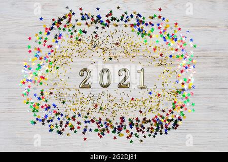 Golden Numbers 2021 entouré d'étoiles dorées et colorées sur fond de bois clair. Le symbole de la nouvelle année. Célébration du nouvel an 2021. Banque D'Images