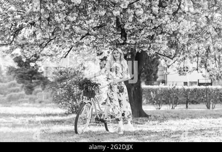 Saison Sakura. Femme avec bouquet de tulipes. Fleurs d'arbre Sakura. Promenade romantique en vélo. Fille robe longue rétro croiseur vélo sakura arbre. Vacances de printemps Banque D'Images