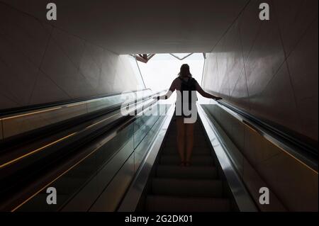 Une femme voyage sur un escalier mécanique dans un bâtiment moderne. Banque D'Images