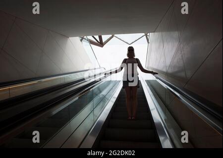 Une femme voyage sur un escalier mécanique dans un bâtiment moderne. Banque D'Images