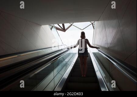 Une femme voyage sur un escalier mécanique dans un bâtiment moderne. Banque D'Images