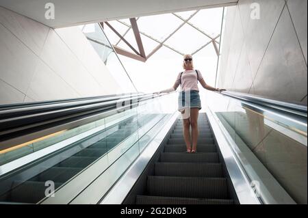 Une femme voyage sur un escalier mécanique dans un bâtiment moderne. Banque D'Images