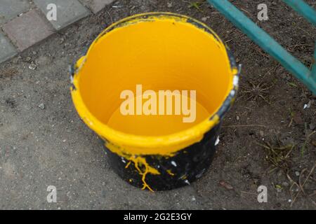 Un seau de peinture jaune. Peinture pour la peinture des poteaux de stationnement. Jaune vif dans un seau en plastique noir. Banque D'Images