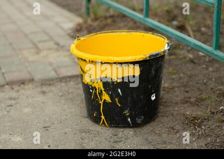 Un seau de peinture jaune. Peinture pour la peinture des poteaux de stationnement. Jaune vif dans un seau en plastique noir. Banque D'Images