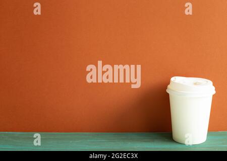 Tasse à café jetable en papier blanc sur table en bois vert. Fond de mur rouge Banque D'Images