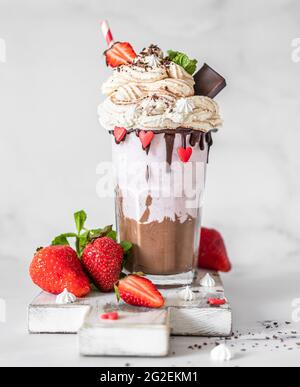 Milkshake au chocolat et à la fraise avec crème glacée et crème fouettée, mini meringue, chocolat, fraise et menthe servis dans un verre. Mise au point sélective. Banque D'Images