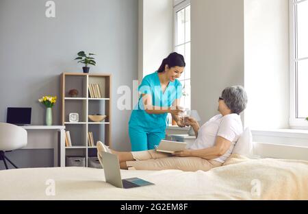Une infirmière donne du verre avec de l'eau à une vieille patiente couchée sur le lit Banque D'Images
