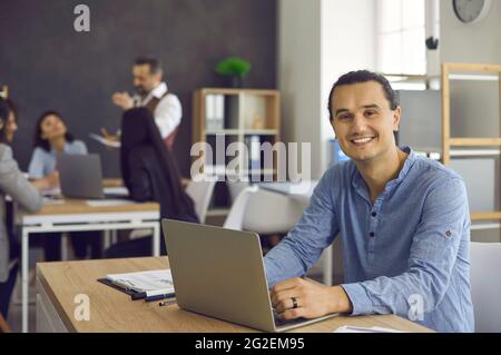 Portrait d'un jeune homme d'affaires heureux assis au bureau avec ordinateur portable Banque D'Images