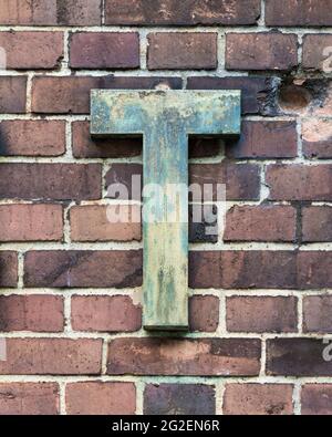 Lettre T en métal abîmé devant un mur de briques Banque D'Images