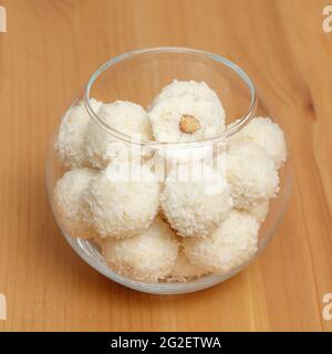 Bonbons végétaliens faits maison. Boules de bonbons blanches avec flocons de noix de coco dans un bol en verre sur fond de bois, gros plan Banque D'Images