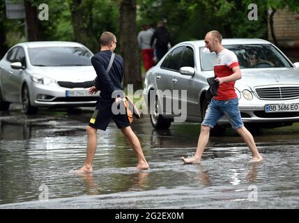 SIEVIERODONETSK, UKRAINE - 10 JUIN 2021 - des hommes Barefoot traversent une rue inondée après une douche à Sievierodonetsk, région de Luhansk, dans l'est de l'Ukraine. Banque D'Images