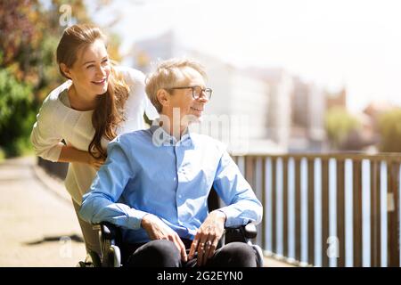 Soins aux personnes âgées et transport en fauteuil roulant. Femme souriante poussant l'homme âgé Banque D'Images