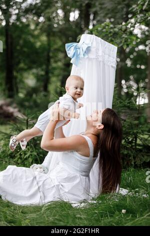 Bonne femme belle, jeune mère jouant et se lancer avec son adorable bébé fils, mignon petit garçon, en appréciant ensemble une journée ensoleillée chaud jouant dessus Banque D'Images