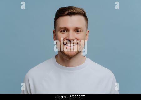 Jeune heureux beau homme non rasé en tenue décontractée souriant à l'appareil photo Banque D'Images