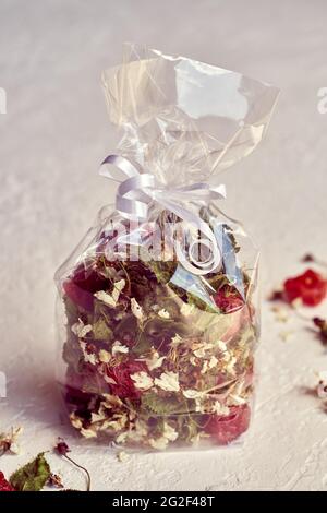 Mélange de thé fait maison à base de cerisiers en fleurs, de jeunes feuilles et de fruits séchés dans un sac de cellophane sur fond blanc Banque D'Images