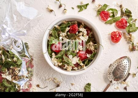 Mélange de thé fait maison à base de cerisiers en fleurs, de jeunes feuilles récoltées au printemps et de fruits séchés dans un bol sur fond blanc Banque D'Images