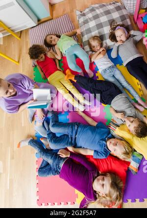 Les enfants actifs s'assetent sur des oreillers et des tapis moelleux à la maternelle Banque D'Images