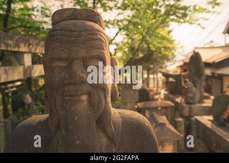 Photo à la tête d'une statue en pierre d'homme sage de style asiatique. Statue dans le cimetière bouddhiste du complexe du sanctuaire de Fushimi-Inari à Kyoto, Japon. Heure d'or Banque D'Images