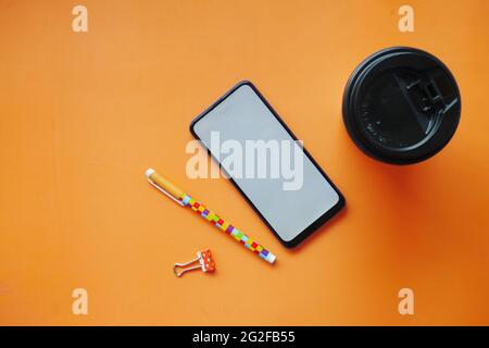 vue de dessus du smartphone, du gobelet à thé et du stylo sur fond orange Banque D'Images