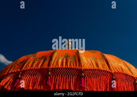 Un gros plan de parasol indien orange vif et or avec des glands roses contre un ciel bleu par une journée ensoleillée Banque D'Images