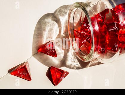 Gros plan d'un dé rouge à 4 faces qui se déverse d'une bouteille en verre sur un bloc-notes. La lumière du soleil qui brille à travers la bouteille crée un beau coeur s Banque D'Images