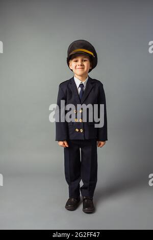 Garçon vêtu d'un uniforme noir de pilote se tient sur fond gris Banque D'Images