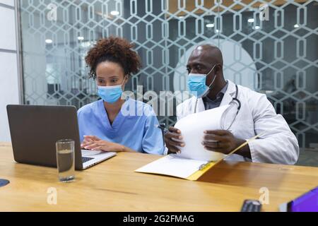 Divers médecins masculins et infirmiers féminins portant des masques faciaux, utilisant un ordinateur portable et parlant Banque D'Images