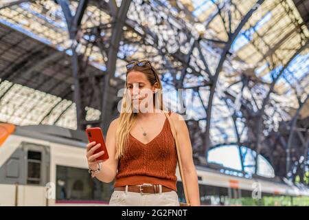 Jeune femme attendant à la plate-forme de la gare à l'aide d'un smartphone Banque D'Images