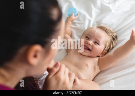 La mère caucasienne embrasse les pieds de son bébé tout en étant assise sur le lit à la maison Banque D'Images