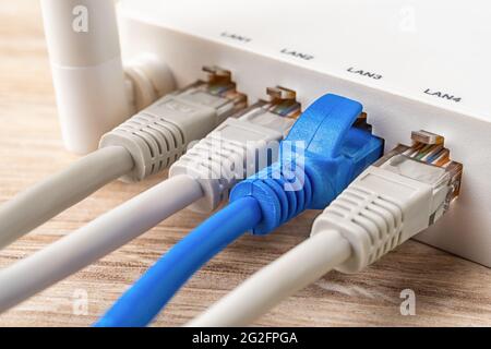Quatre câbles réseau connectés au routeur sans fil Wi-Fi blanc sur un bureau en bois. Macro du routeur wlan domestique et professionnel fournit une connexion Internet. Banque D'Images