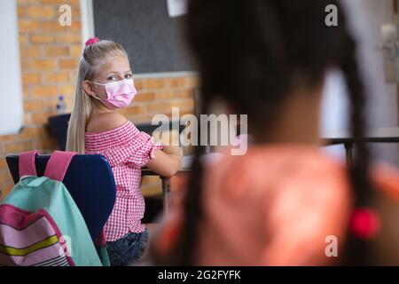 Une fille caucasienne portant un masque facial assise sur son bureau en classe à l'école Banque D'Images