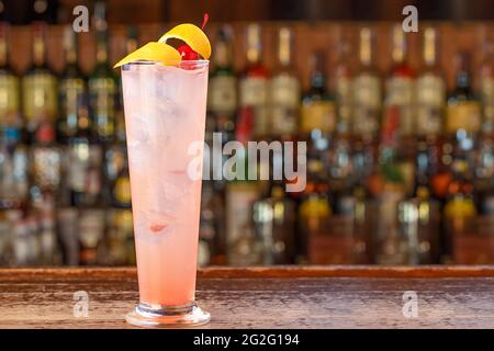 Cocktail alcoolisé glamour au bar. Une boisson rose avec beaucoup de glace, et une belle garniture de zeste de citron et de cerise Banque D'Images