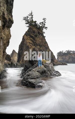Femme debout sur les rochers à côté de l'océan avec des vagues laiteuses lisses Banque D'Images