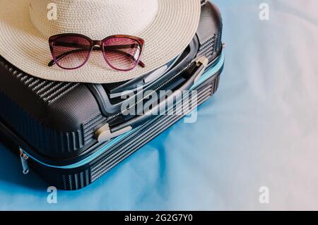 Valise élégante avec lunettes de soleil et passeport sur fond bleu, vue du dessus Banque D'Images