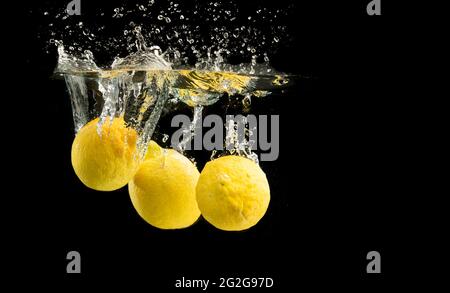 Des citrons jaunes frais dans l'eau éclabousser sur fond noir Banque D'Images