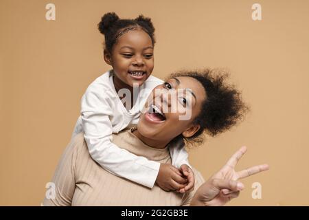 Bonne mère noire et fille riant tout en montrant le signe de paix isolé sur fond beige Banque D'Images