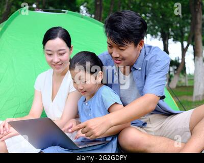 Une famille heureuse de trois personnes utilise un ordinateur pour surfer sur Internet en plein air de haute qualité photo Banque D'Images