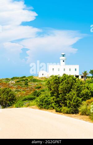 Vue imprenable un phare blanc entouré d'une végétation verte pendant une belle journée ensoleillée avec une route en premier plan. Cala Del Faro, Sardaigne. Banque D'Images