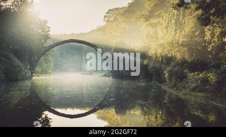 Lever de soleil en automne derrière le Rakotzbrücke historique dans le parc Kromlau Rhododendron. Banque D'Images