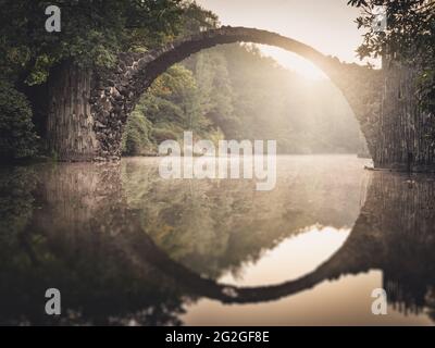 Lever de soleil en automne derrière le Rakotzbrücke historique dans le parc Kromlau Rhododendron. Banque D'Images