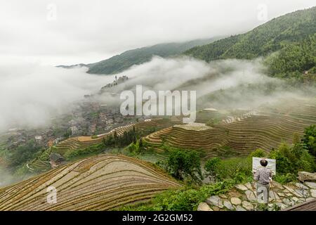 Un artiste peint le paysage élevé des champs de riz lors d'une journée de brouillard à Longsheng Rice Terraces, Longji, Chine Banque D'Images