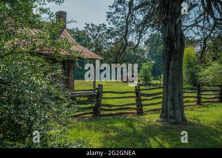 Vue partielle sur la maison abandonnée avec une clôture rustique en décomposition entourant la propriété et l'équipement de ferme ancien laissé en arrière-plan sur un su lumineux Banque D'Images